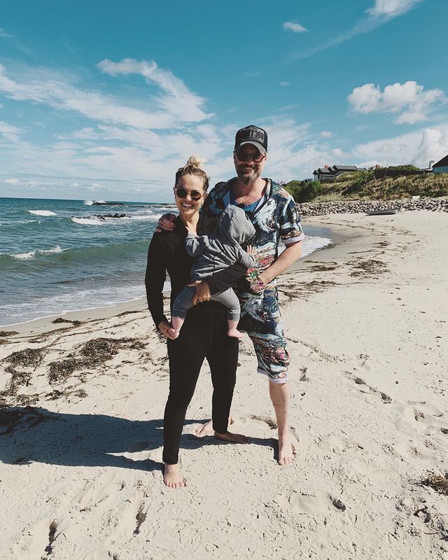 Emilie Ullerup carrying her son on the beach along her husband.